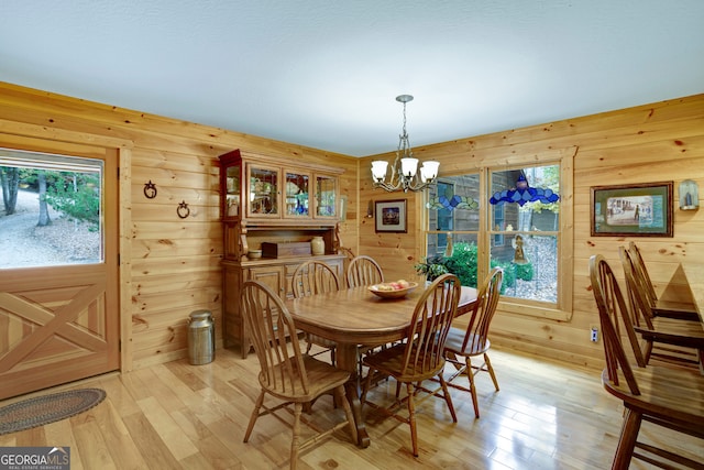 dining room with wood walls, a chandelier, and light hardwood / wood-style floors