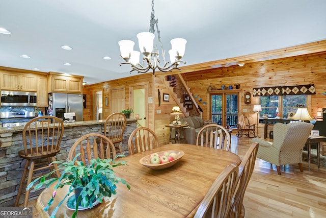 dining space featuring a notable chandelier, french doors, wooden walls, and light hardwood / wood-style flooring