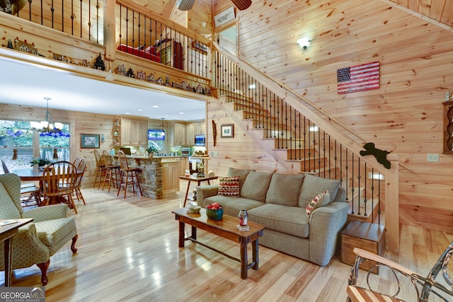 living room with wood walls, a towering ceiling, ceiling fan with notable chandelier, and light wood-type flooring