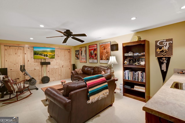 living room featuring ceiling fan, wood walls, light colored carpet, and sink