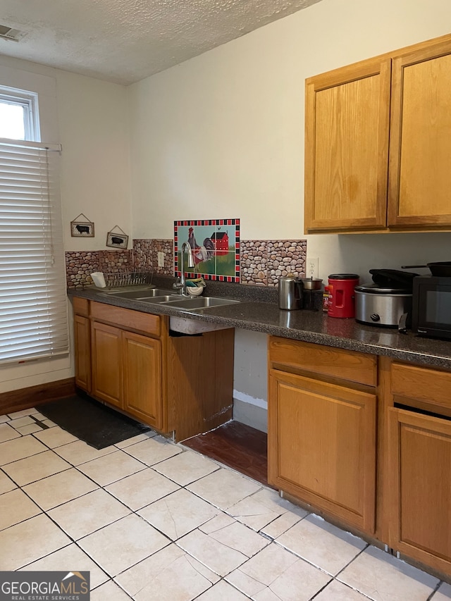 kitchen featuring sink, decorative backsplash, a textured ceiling, and light tile patterned floors