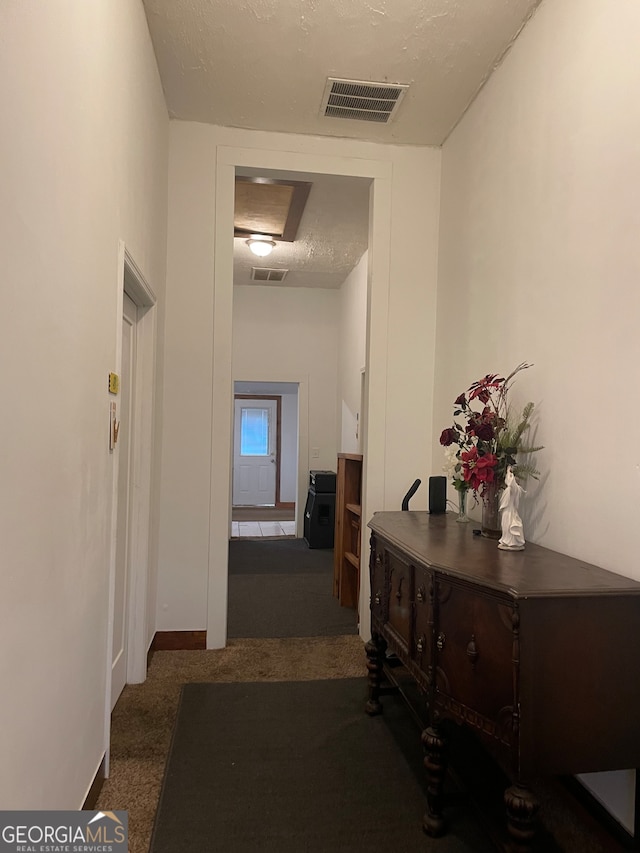 hallway with dark colored carpet and a textured ceiling