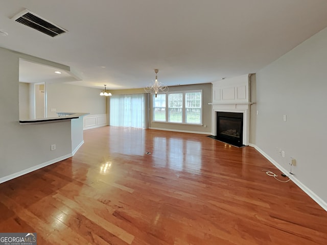 unfurnished living room featuring a large fireplace, light hardwood / wood-style floors, and an inviting chandelier