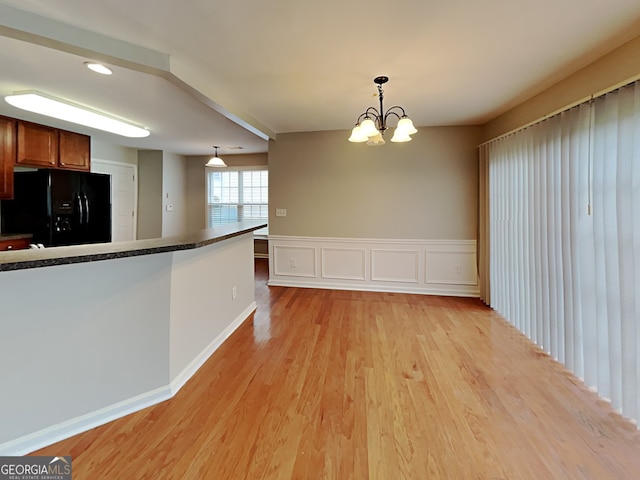 kitchen featuring light hardwood / wood-style floors, a notable chandelier, decorative light fixtures, and black fridge