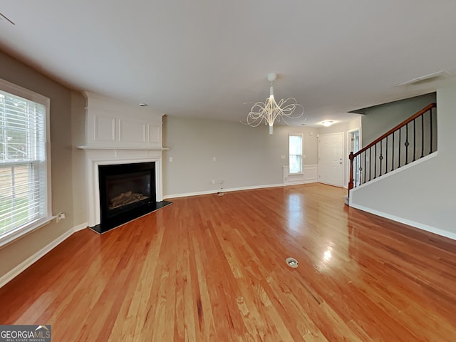 unfurnished living room with light hardwood / wood-style floors, a notable chandelier, and a fireplace