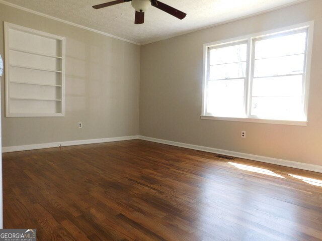 spare room featuring baseboards, visible vents, dark wood-type flooring, and crown molding