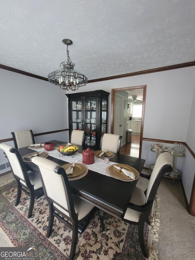 dining space with carpet floors, ornamental molding, a textured ceiling, and a notable chandelier