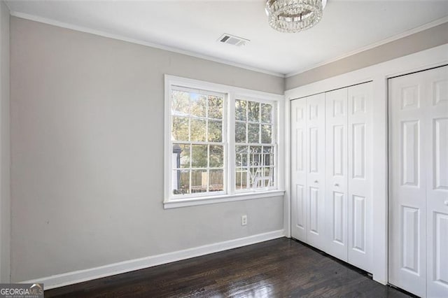 unfurnished bedroom with ornamental molding, an inviting chandelier, multiple closets, and dark wood-type flooring