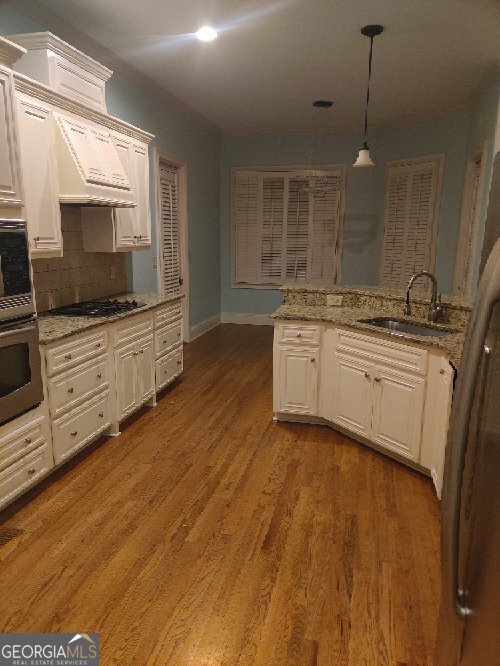 kitchen featuring white cabinets, custom range hood, stainless steel appliances, and sink