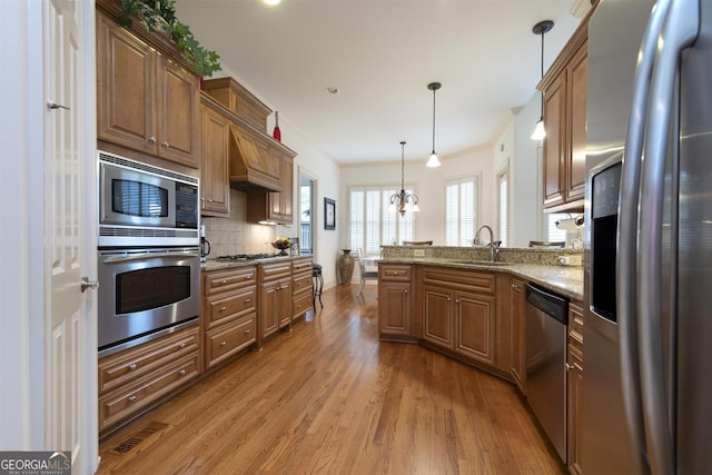 kitchen with light stone countertops, ornamental molding, stainless steel appliances, decorative light fixtures, and hardwood / wood-style flooring