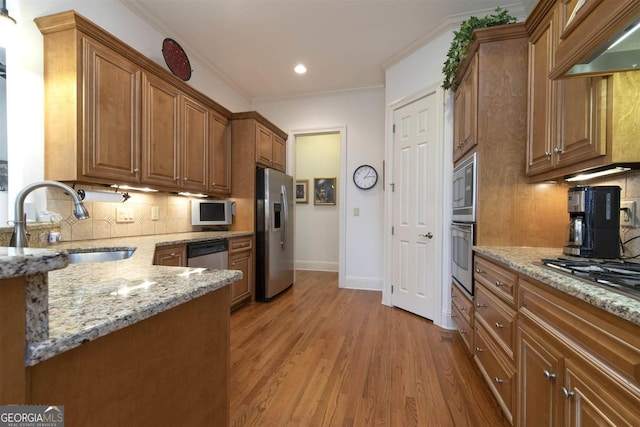 kitchen featuring sink, light stone counters, backsplash, light hardwood / wood-style floors, and appliances with stainless steel finishes