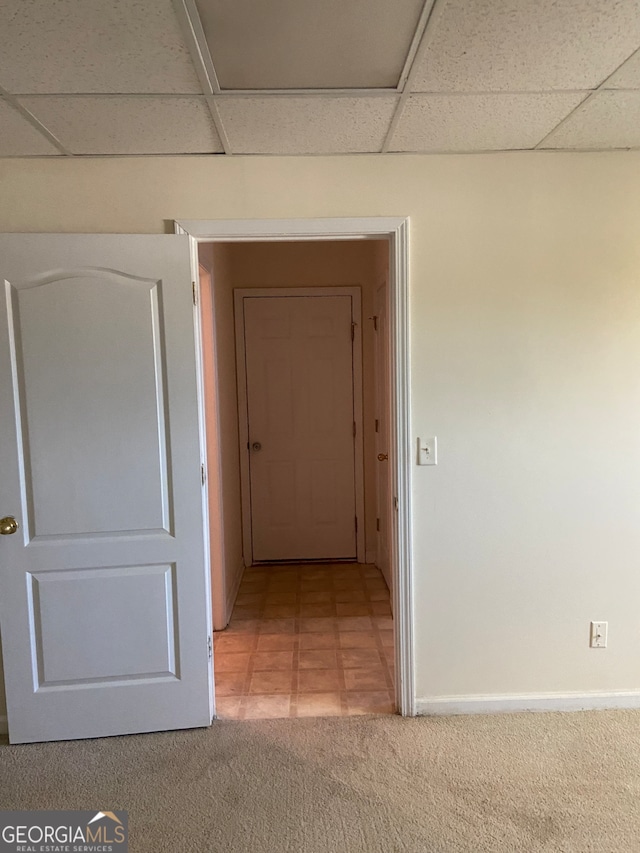 hallway with light colored carpet and a paneled ceiling