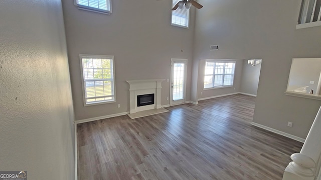 unfurnished living room with a towering ceiling, wood-type flooring, and ceiling fan