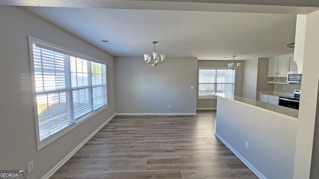 unfurnished dining area with a wealth of natural light, dark hardwood / wood-style floors, and a notable chandelier