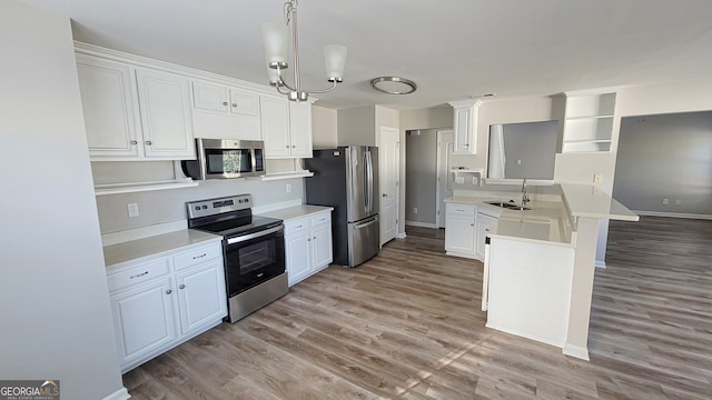 kitchen featuring appliances with stainless steel finishes, hanging light fixtures, sink, white cabinets, and light hardwood / wood-style flooring