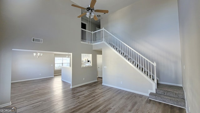 unfurnished living room with hardwood / wood-style floors, ceiling fan with notable chandelier, and a towering ceiling