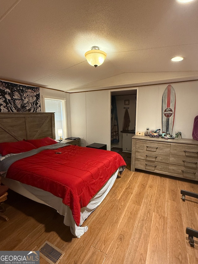 bedroom featuring lofted ceiling, hardwood / wood-style floors, and a textured ceiling