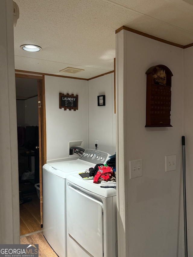 clothes washing area featuring ornamental molding, a textured ceiling, washing machine and dryer, and light wood-type flooring