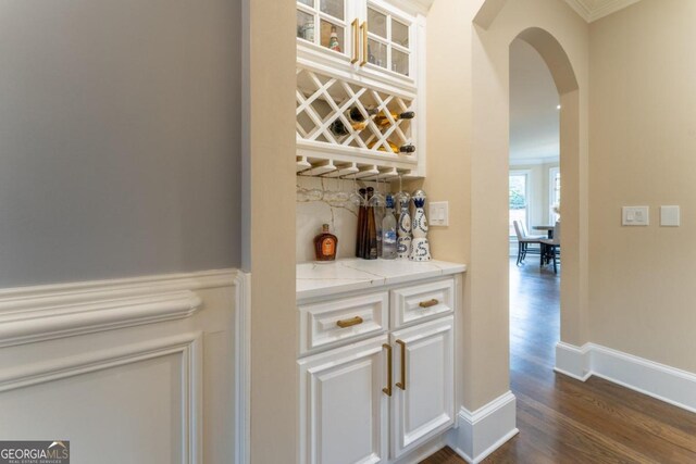 bar with dark wood-type flooring, light stone counters, ornamental molding, and white cabinets