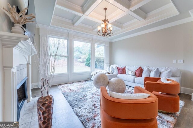 living room featuring beam ceiling, an inviting chandelier, ornamental molding, a tile fireplace, and coffered ceiling