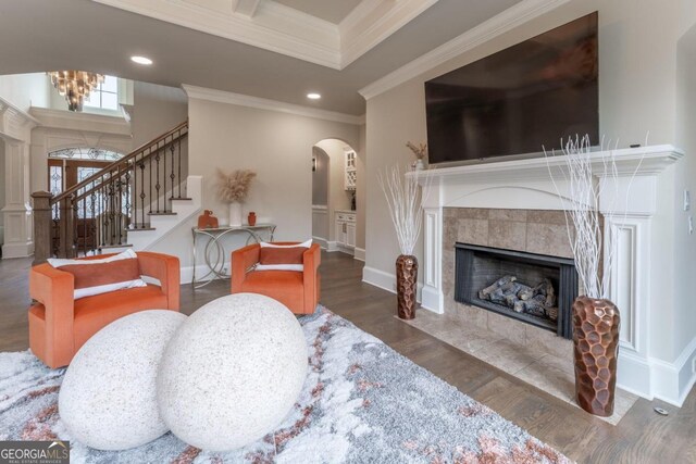 living room with dark wood-type flooring, a notable chandelier, ornamental molding, and a fireplace