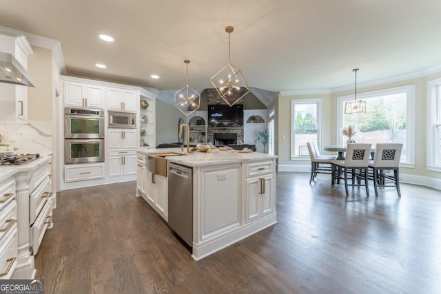 kitchen with white cabinets, an island with sink, appliances with stainless steel finishes, decorative light fixtures, and sink