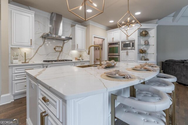 kitchen with wall chimney exhaust hood, white cabinets, tasteful backsplash, and an island with sink