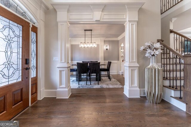 entrance foyer featuring crown molding, a chandelier, ornate columns, and dark hardwood / wood-style flooring