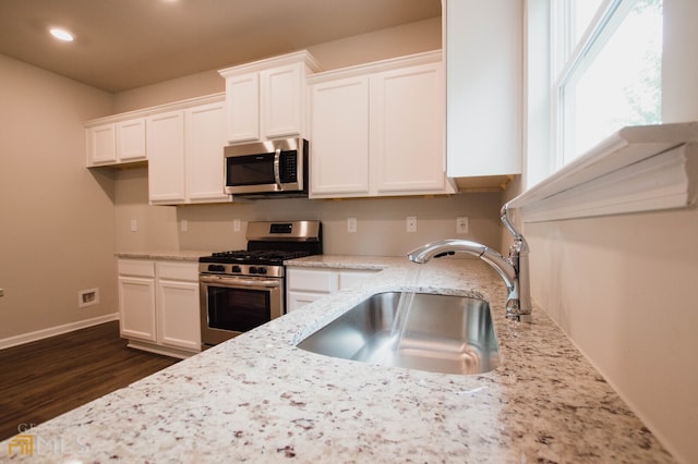 kitchen with light stone counters, dark hardwood / wood-style flooring, appliances with stainless steel finishes, white cabinetry, and sink