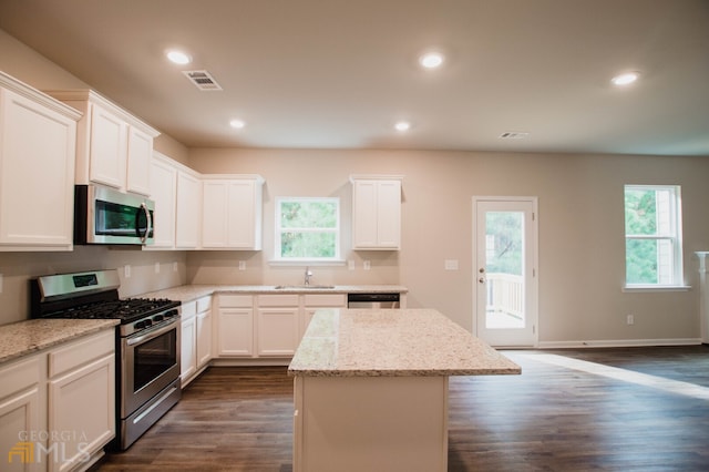 kitchen with appliances with stainless steel finishes, white cabinets, dark wood-type flooring, and a kitchen island