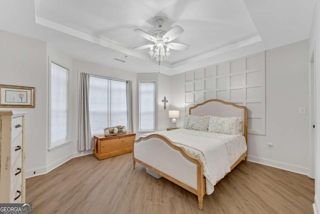 bedroom with light wood-type flooring, a tray ceiling, and ceiling fan