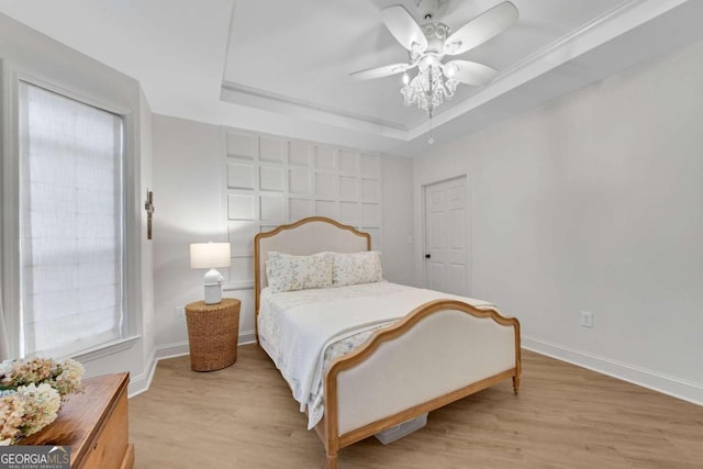 bedroom with a tray ceiling, ceiling fan, and light hardwood / wood-style flooring