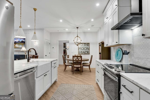 kitchen with wall chimney exhaust hood, light stone counters, pendant lighting, white cabinets, and appliances with stainless steel finishes