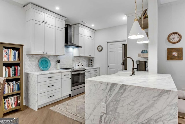 kitchen featuring light stone counters, wall chimney exhaust hood, electric range, white cabinets, and hanging light fixtures