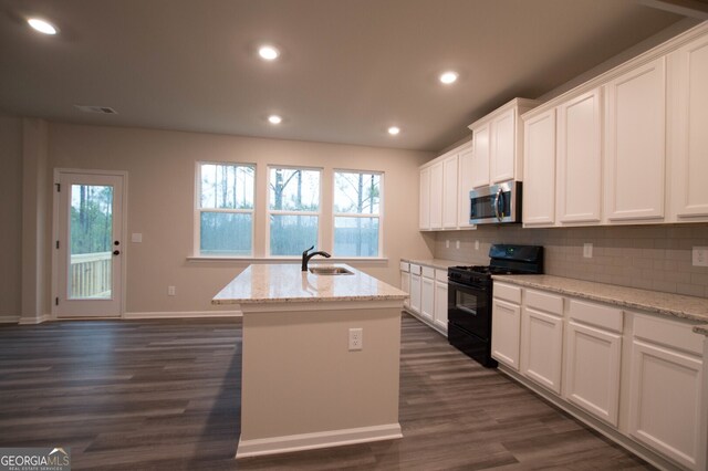 kitchen with dark wood-type flooring, gas stove, a center island with sink, and white cabinets