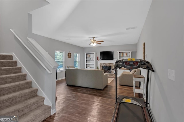 living room featuring ceiling fan, dark wood-type flooring, and a brick fireplace