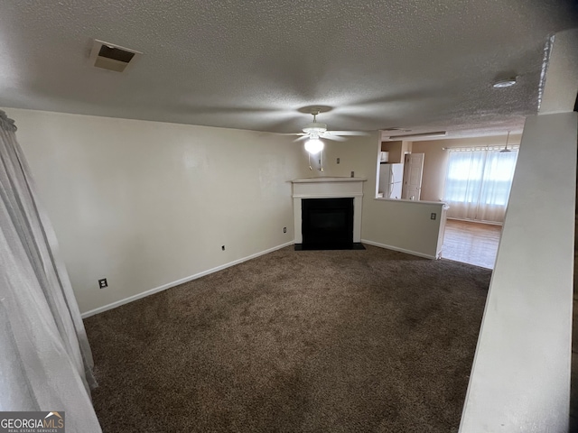 unfurnished living room with ceiling fan, a textured ceiling, and dark carpet