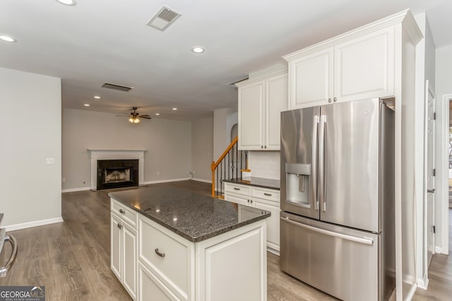 kitchen with ceiling fan, a kitchen island, stainless steel fridge with ice dispenser, wood-type flooring, and dark stone counters