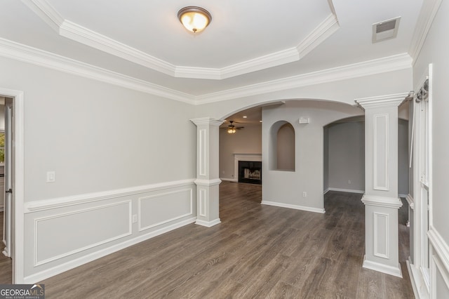 empty room featuring a tray ceiling, dark hardwood / wood-style flooring, ornate columns, ceiling fan, and crown molding