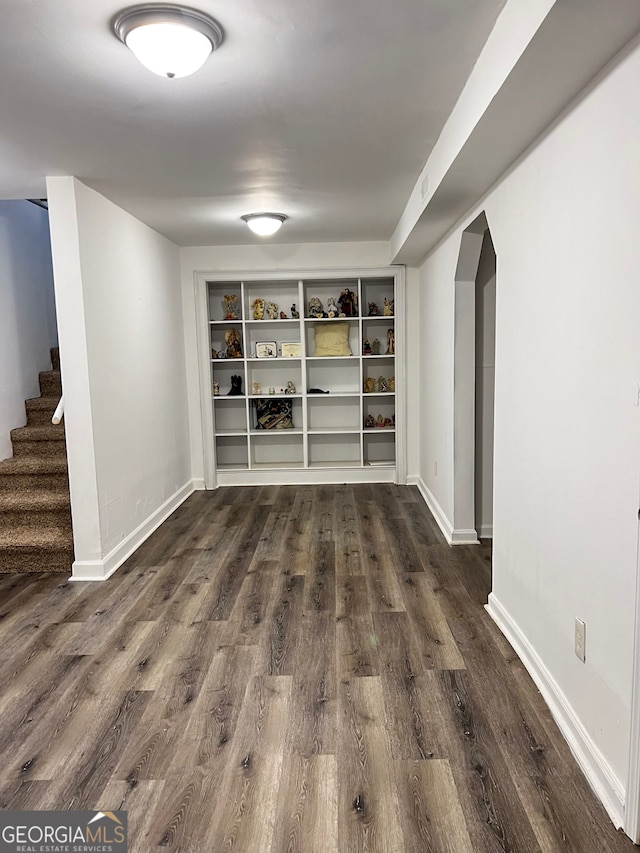 interior space with arched walkways, dark wood finished floors, stairs, and baseboards