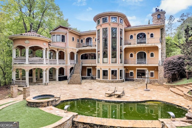 rear view of house with a balcony, an in ground hot tub, and a patio area