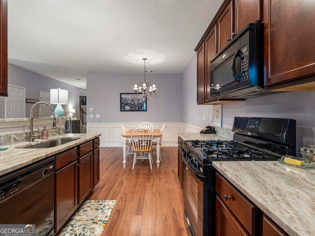 kitchen with black appliances, sink, light hardwood / wood-style floors, pendant lighting, and an inviting chandelier