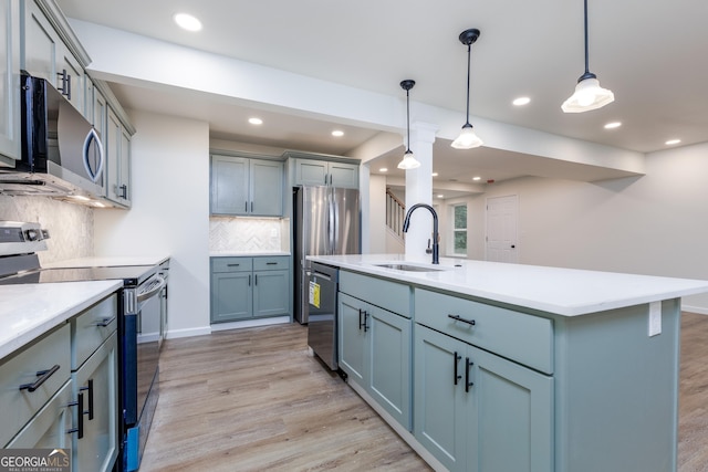 kitchen featuring sink, a center island with sink, light hardwood / wood-style flooring, pendant lighting, and stainless steel appliances