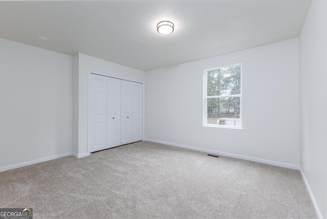 unfurnished bedroom with light colored carpet and a closet