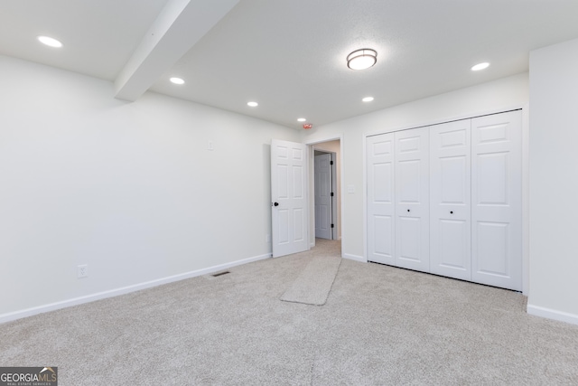 unfurnished bedroom featuring beamed ceiling, light colored carpet, and a closet