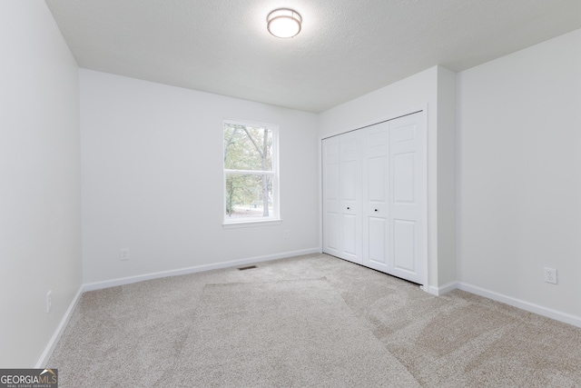 unfurnished bedroom featuring light colored carpet, a closet, and a textured ceiling