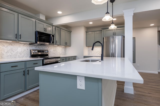 kitchen with pendant lighting, sink, stainless steel appliances, and an island with sink