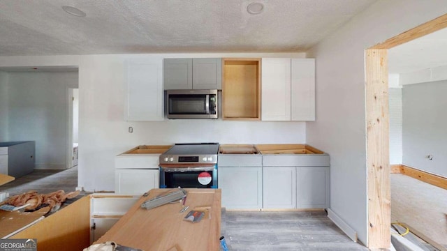 kitchen with light hardwood / wood-style floors, appliances with stainless steel finishes, a textured ceiling, and white cabinets