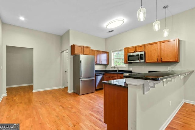 kitchen featuring kitchen peninsula, a breakfast bar, light hardwood / wood-style flooring, stainless steel appliances, and decorative light fixtures