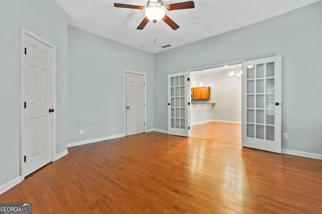 spare room featuring french doors, light hardwood / wood-style flooring, and ceiling fan with notable chandelier